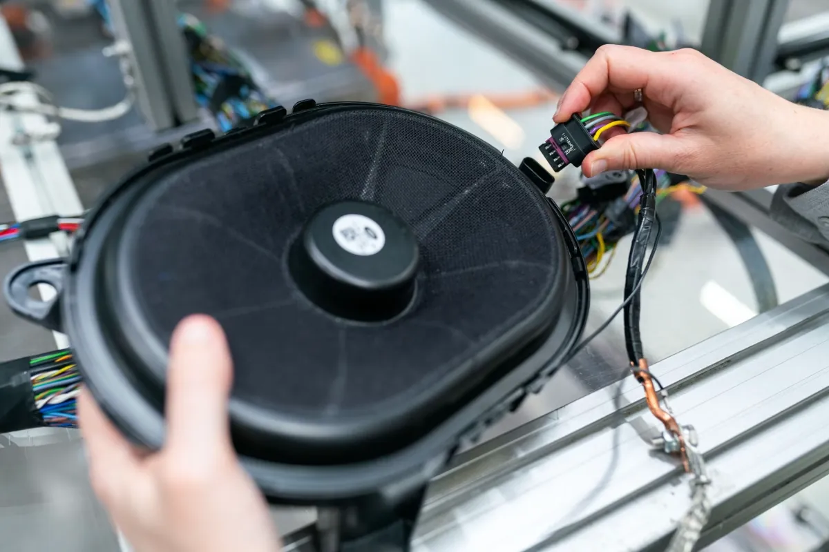 Hands connecting a wiring harness to a car speaker on an assembly line